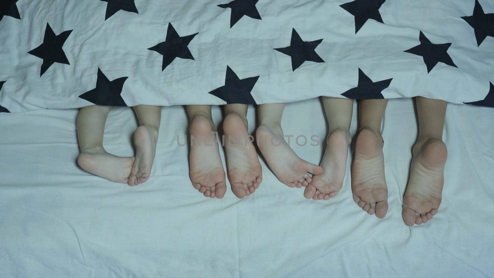 Legs of babies in the bed from under the covers before going to bed. by DovidPro