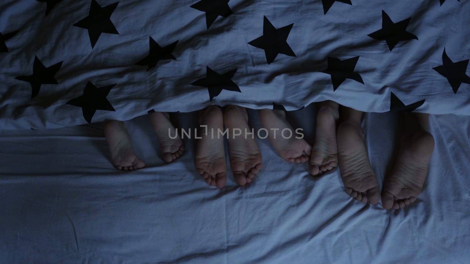 Legs of babies in the bed from under the covers before going to bed. by DovidPro