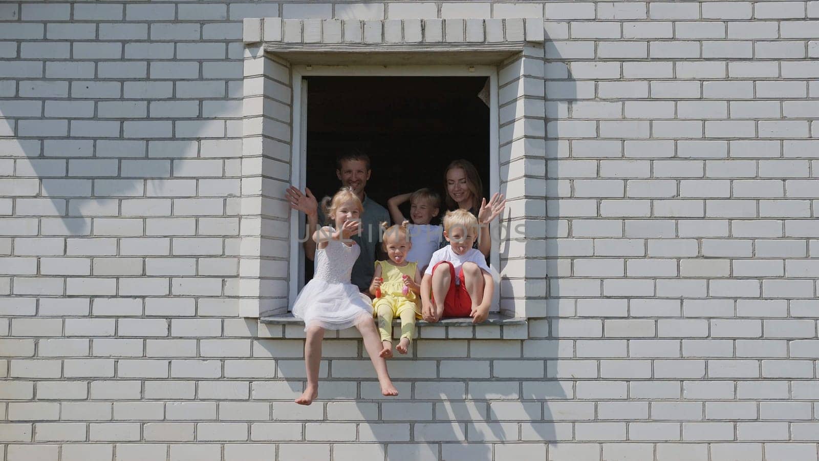 The concept of a large family. A friendly family waves their hands from the window of their home. by DovidPro