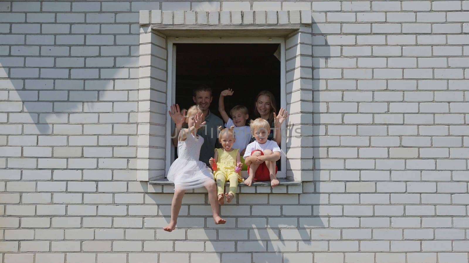 The concept of a large family. A friendly family waves their hands from the window of their home. by DovidPro
