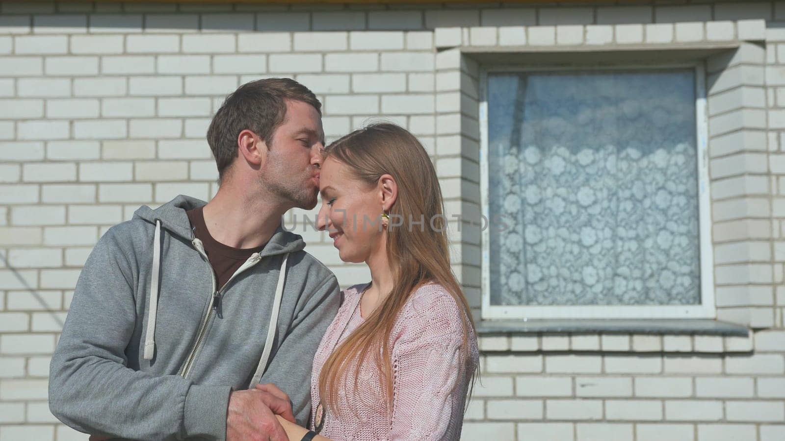 A loving husband kisses his wife in front of his house