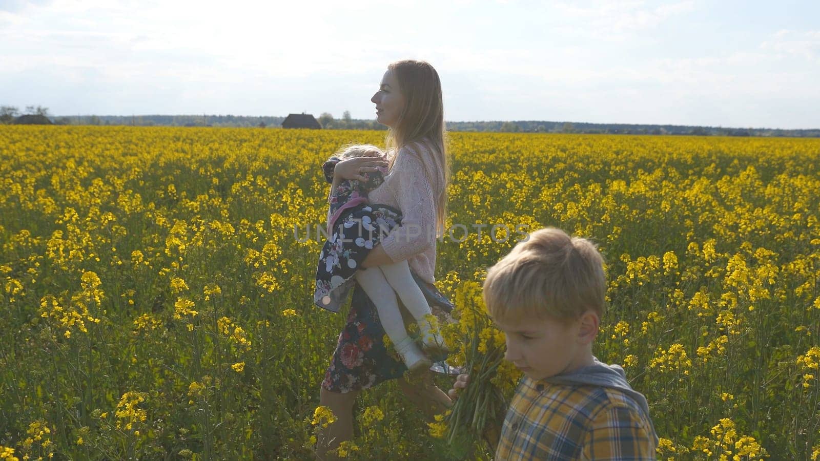 Happy mother with children walks on a rapeseed field