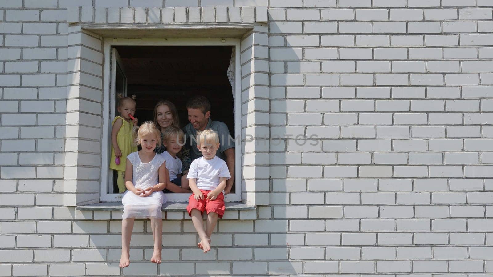 The concept of a large family. A family of 6 waves their hands from the window of their house