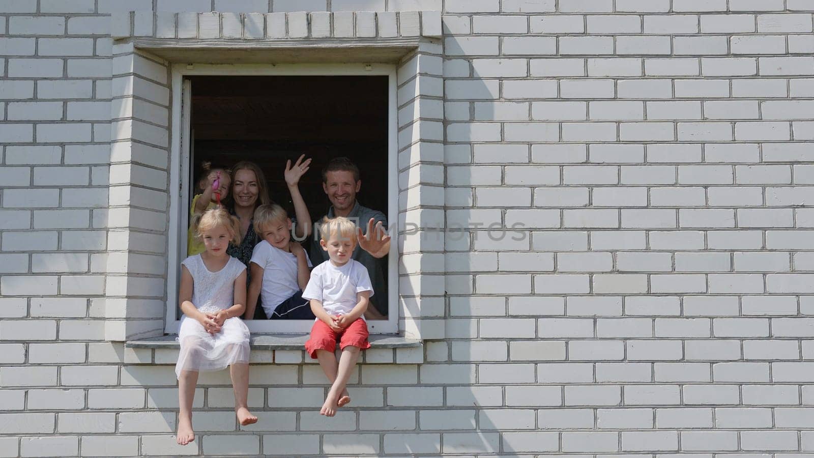 A large family waves their hands and hides from the window of their home. by DovidPro