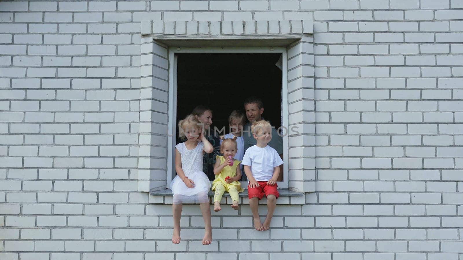 A large large family poses from the window of their home