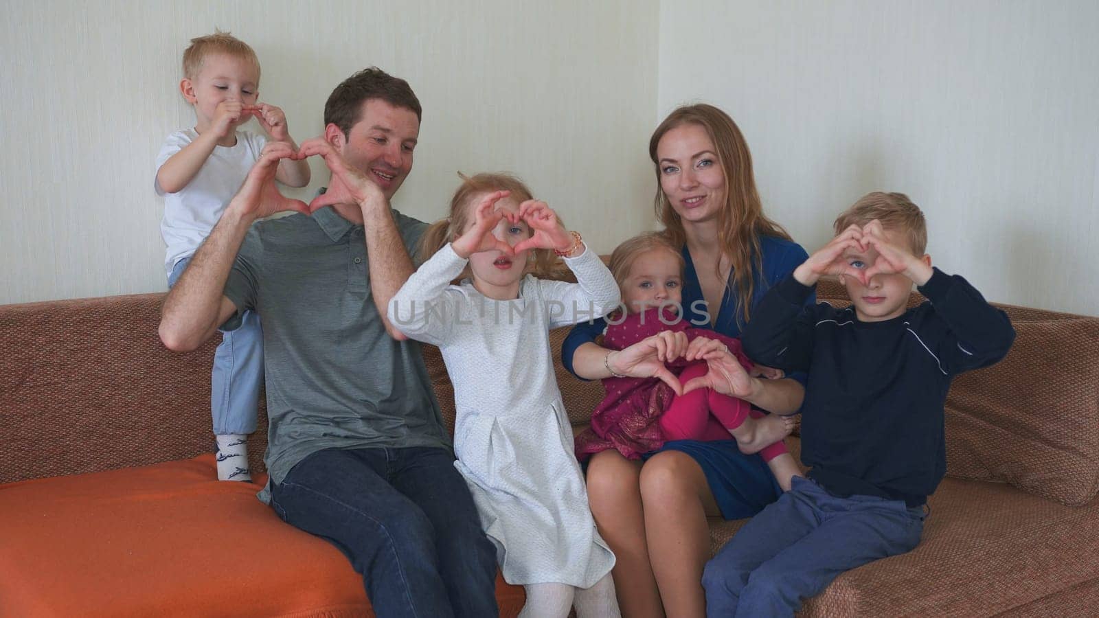 Big friendly family on the couch make hearts out of their hands