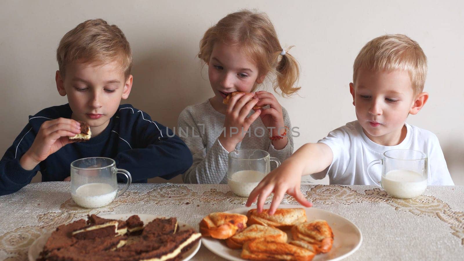 Mother serves cookies on the table and the children eat it with milk. by DovidPro