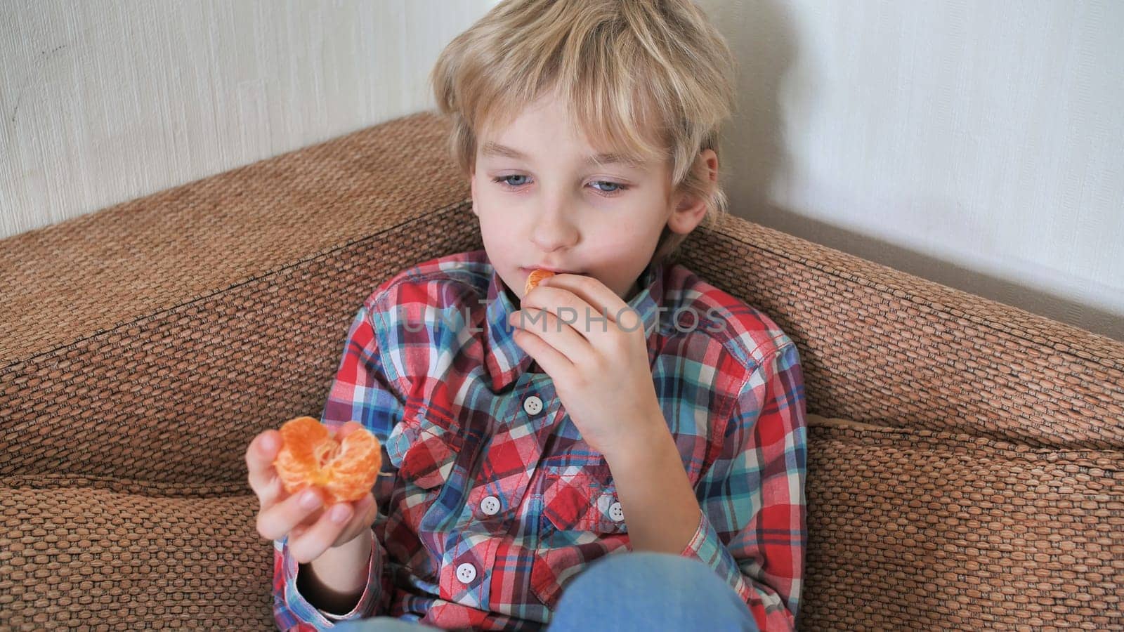 Eight year old boy eats mandarin at home.