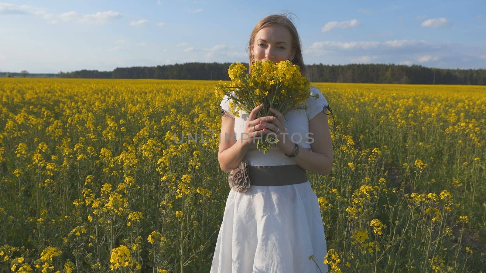 A girl in a white dress is walking among a rapeseed field