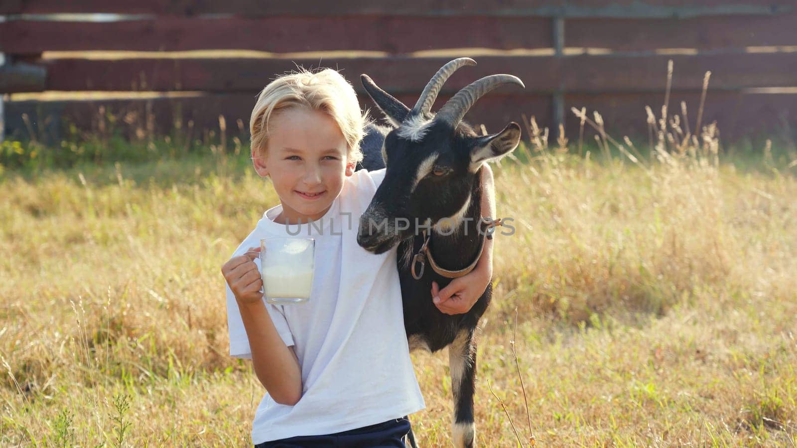 A boy drinks goat milk from a mug next to his goat. by DovidPro