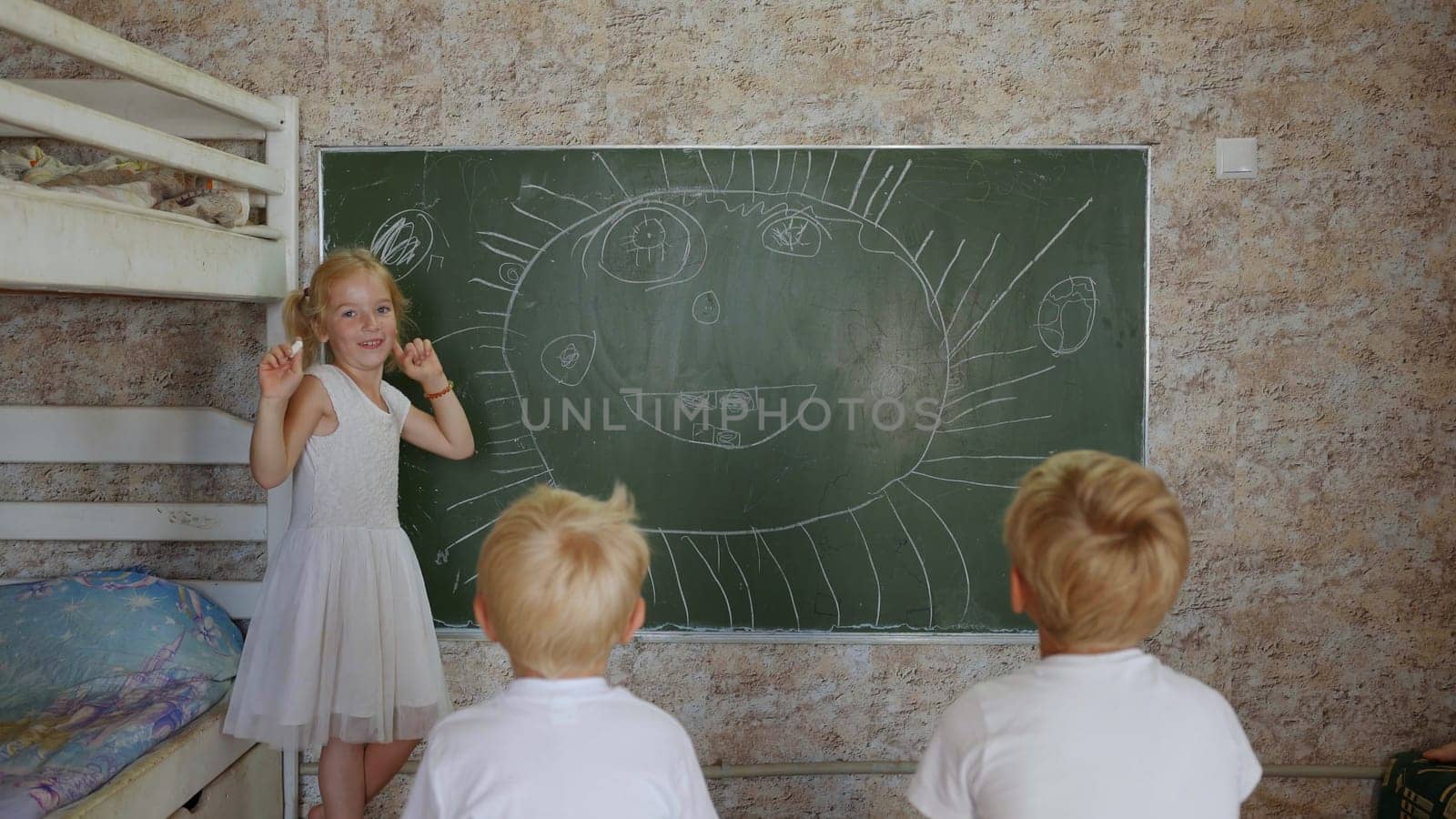 A six year old girl draws on a board in front of her brothers