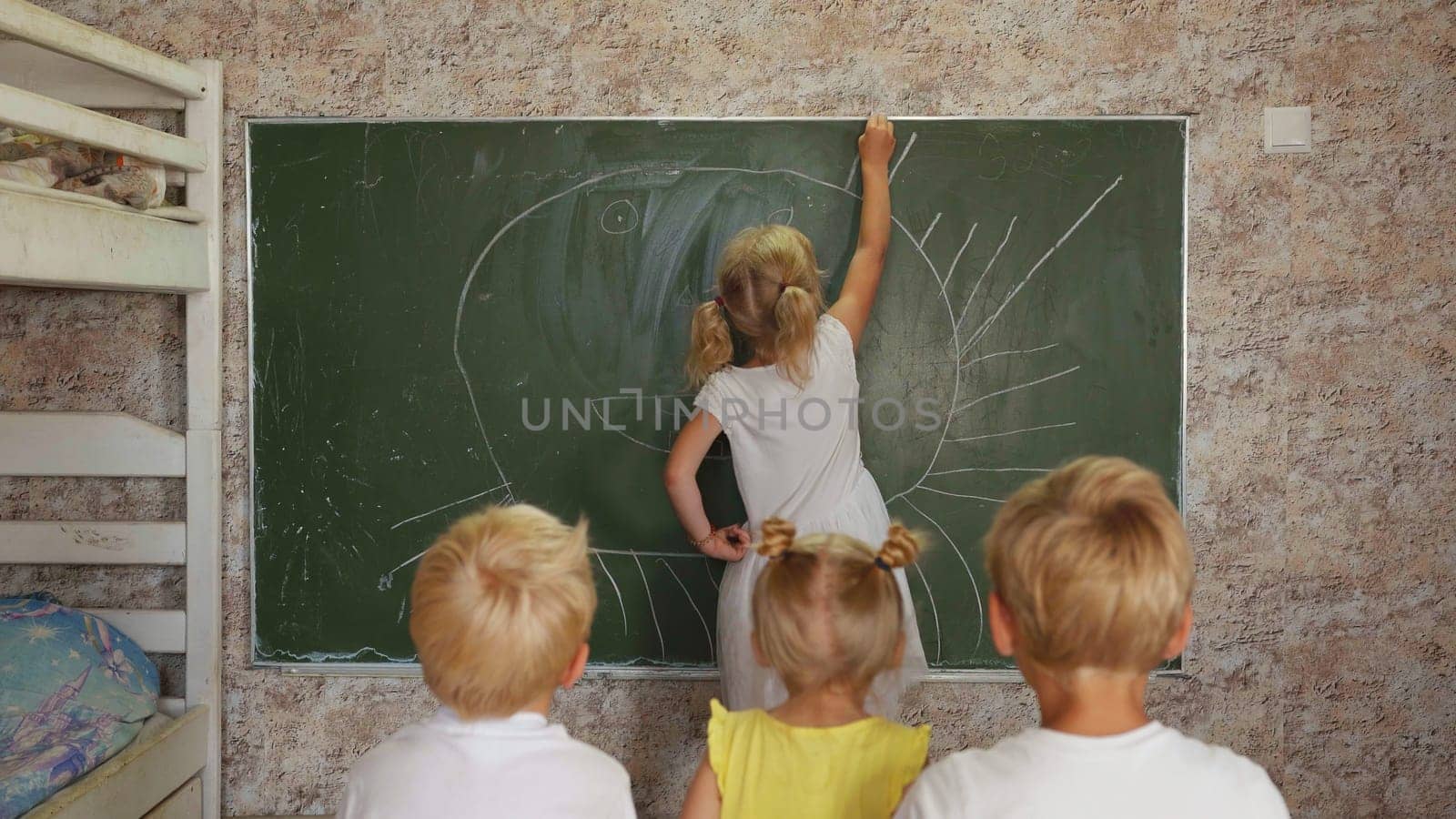 A six year old girl draws on a board in front of her sisters and brothers