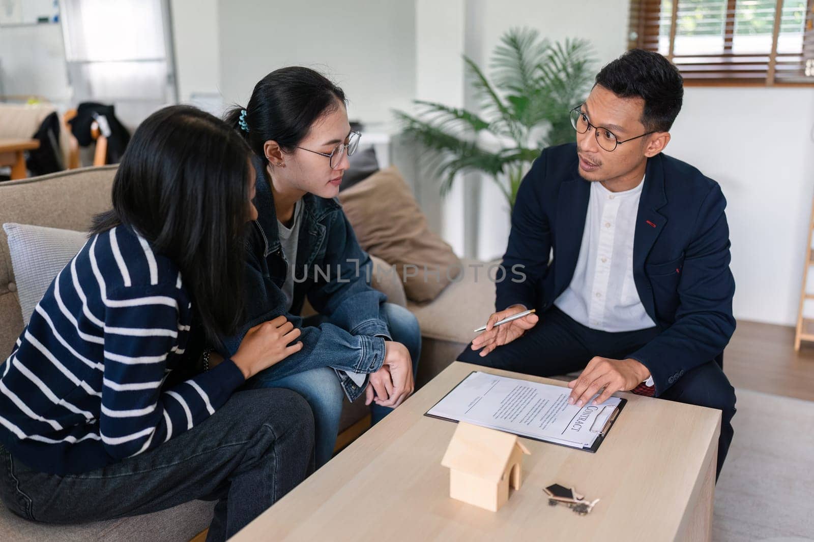 young lesbian married couple discussing agreement with real estate agent or broker. Professional financial advisor or saleswoman explaining contract detail.