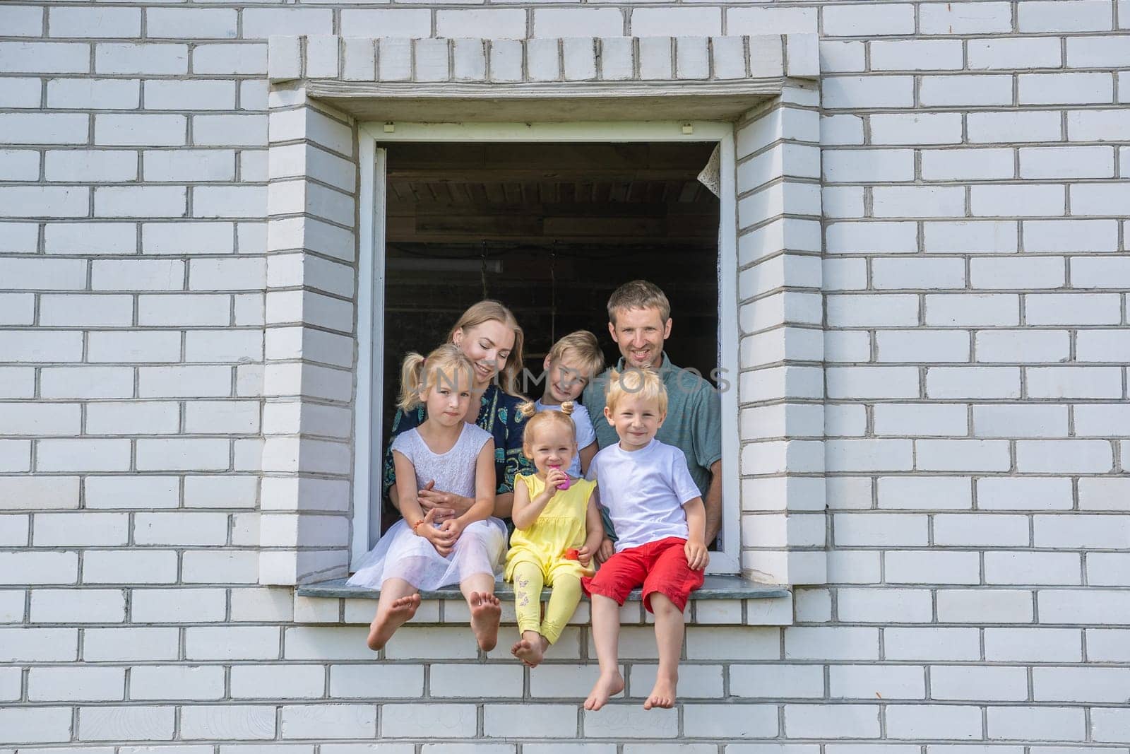 A large large family poses from the window of their home