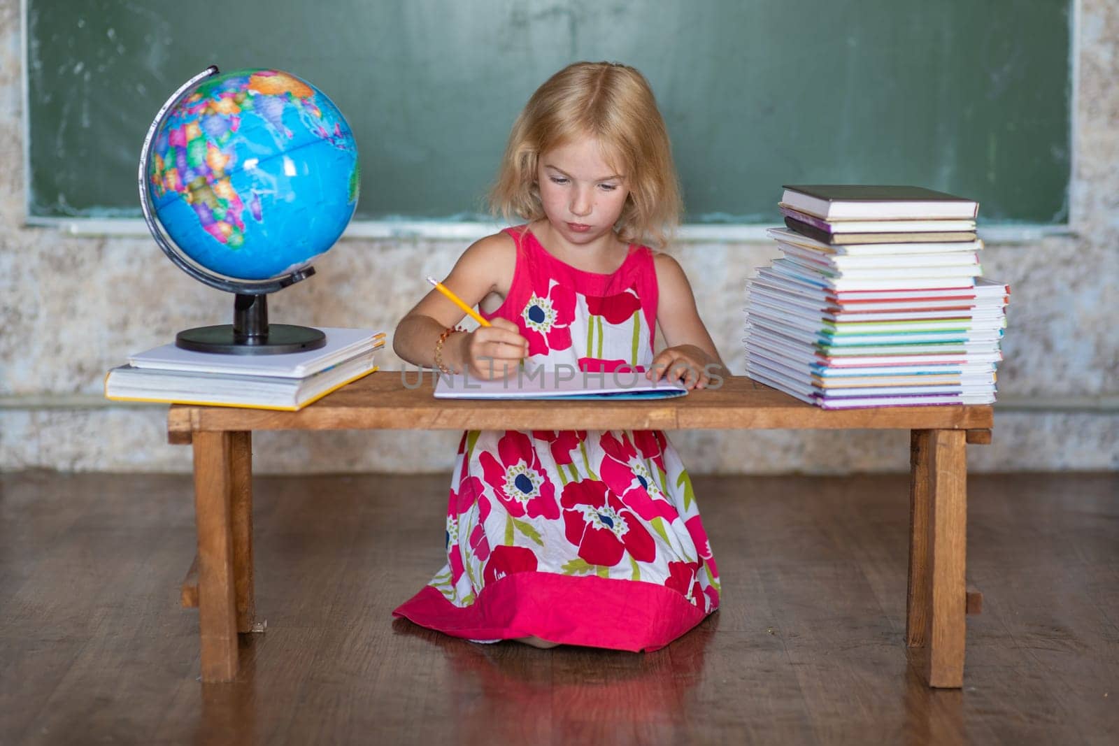 Little girl teaches home lessons on a bench against the background of the globe and books