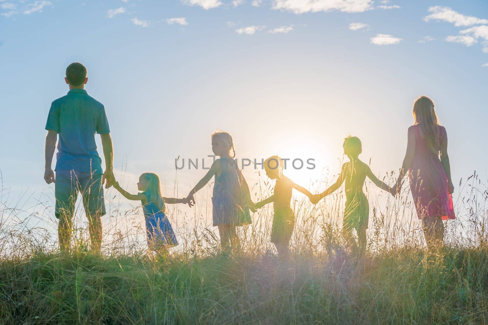 A large family is standing holding hands against the background of the sunset