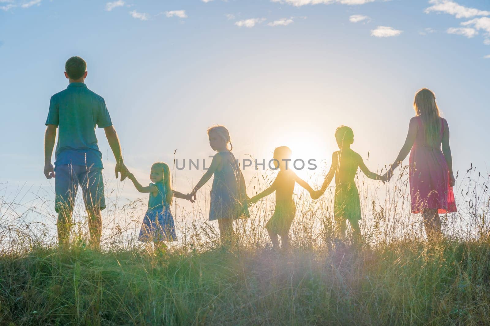 A large family is standing holding hands against the background of the sunset. by DovidPro