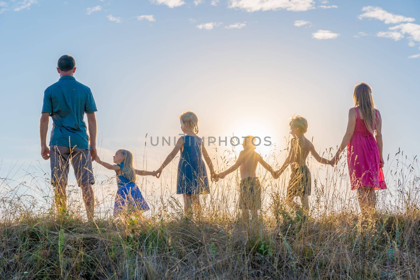 A large family is standing holding hands against the background of the sunset. by DovidPro