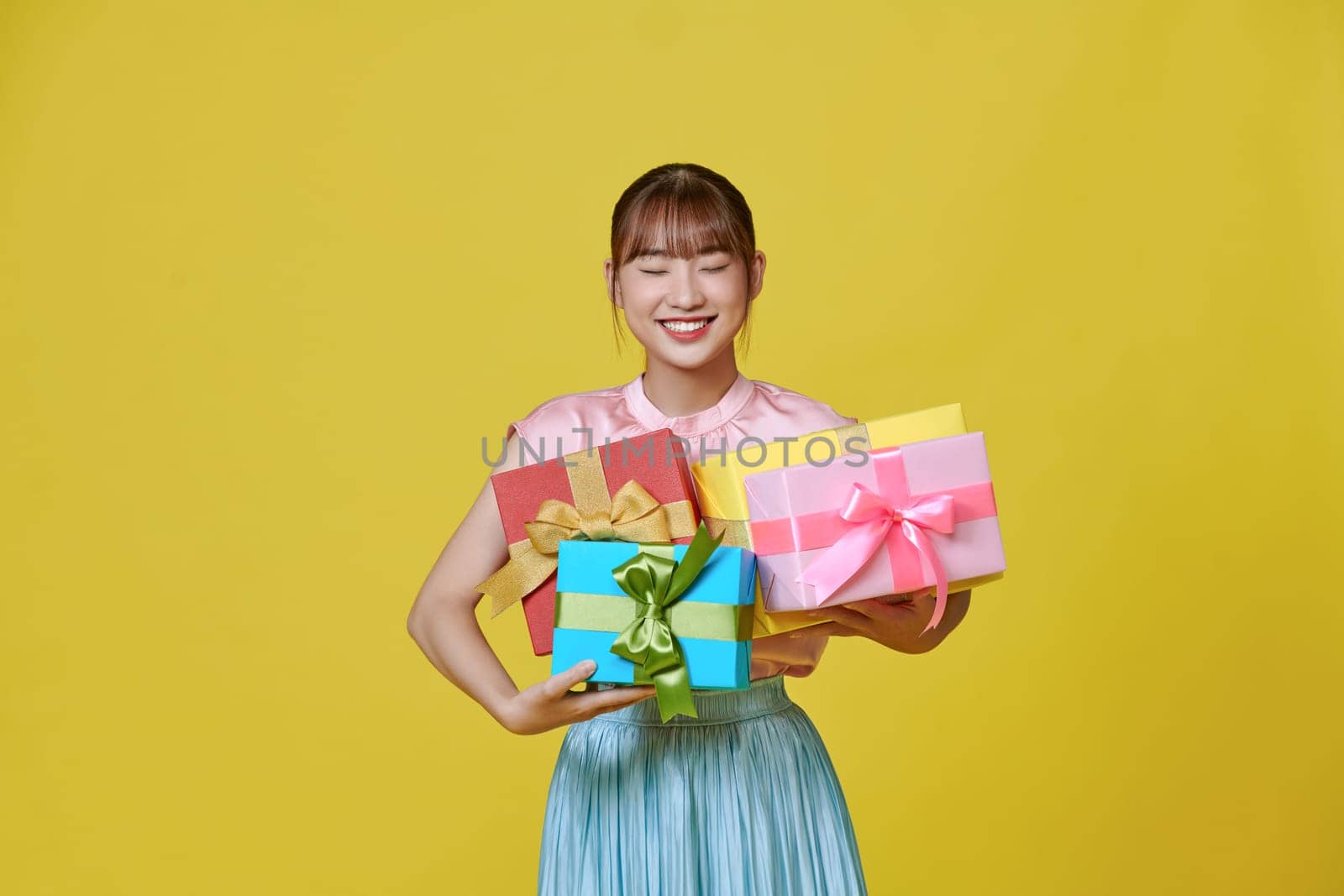 Happy cheerful girl likes celebrating birthday and receive presents, holding a pile of gift boxes