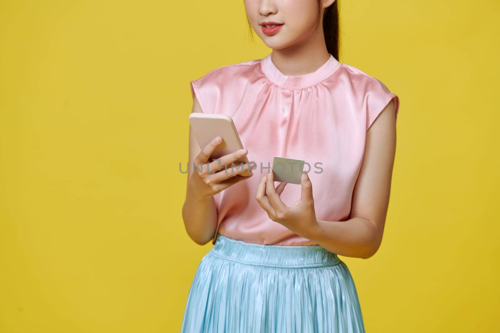 Portrait of a smiling woman holding credit card and mobile phone over yellow background by makidotvn