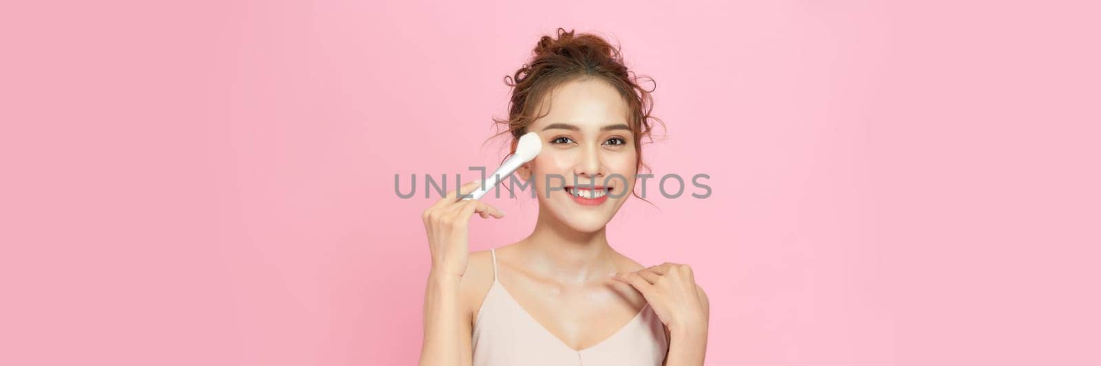 Closeup portrait of beautiful happy young girl with perfect skin is holding makeup brush in hand.