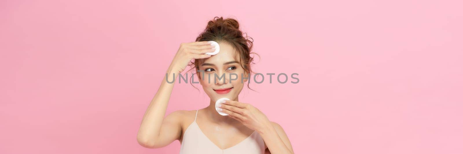 Smiling pretty young woman cleaning her face, using cotton pads and cleansing product by makidotvn