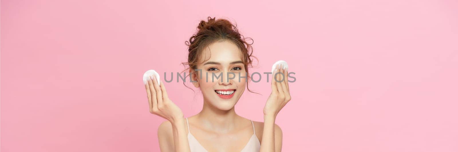 Smiling pretty young woman cleaning her face, using cotton pads and cleansing product