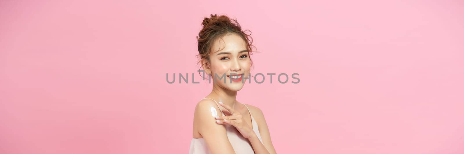 Beautiful young asian woman happy applying cream or lotion with moisturizer to skin on shoulder by makidotvn