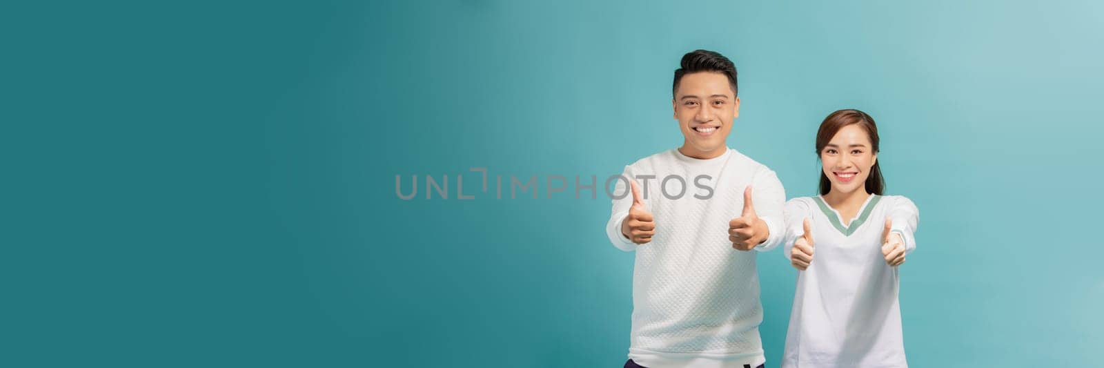 Photo of happy excited young loving couple standing isolated, showing thumbs up gesture. by makidotvn