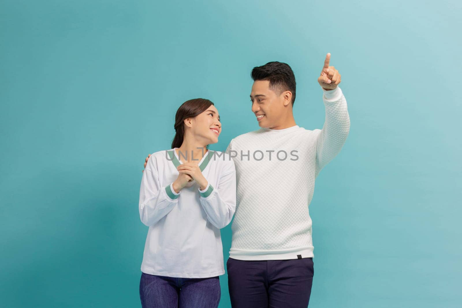 Young couple together with a big smile on face, pointing with hand finger to the side