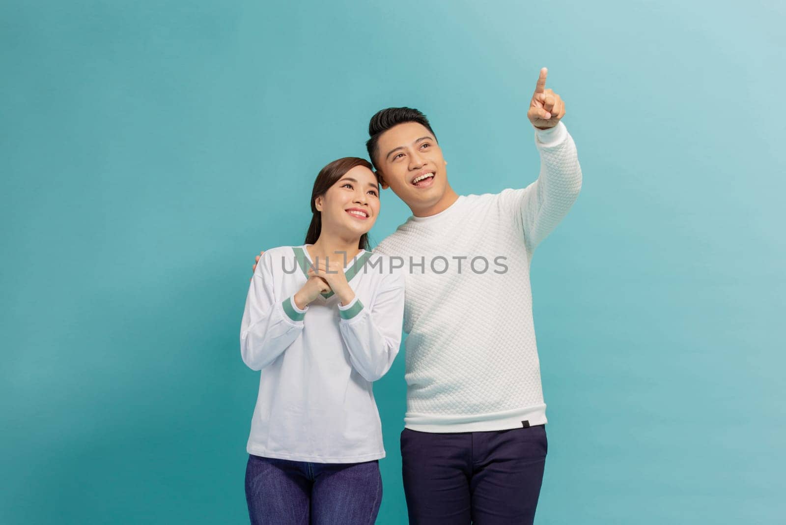 Young couple together with a big smile on face, pointing with hand finger to the side by makidotvn