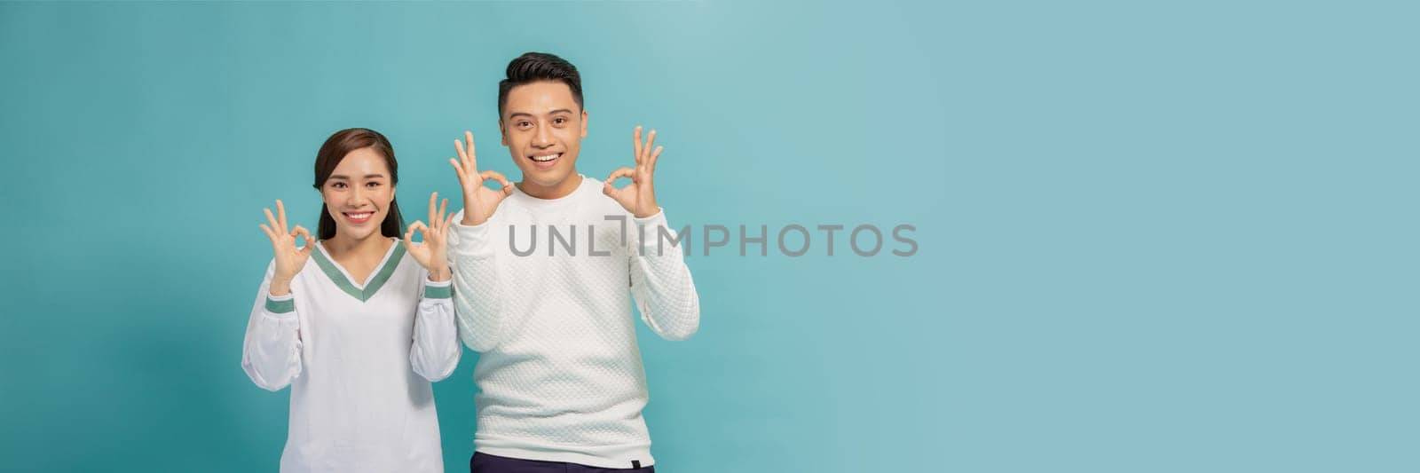 Portrait of young Asian couple showing ok sign isolated on  blue background, Two people concept by makidotvn