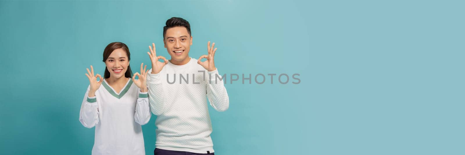 Young couple standing together smiling positive doing ok sign with hand and fingers