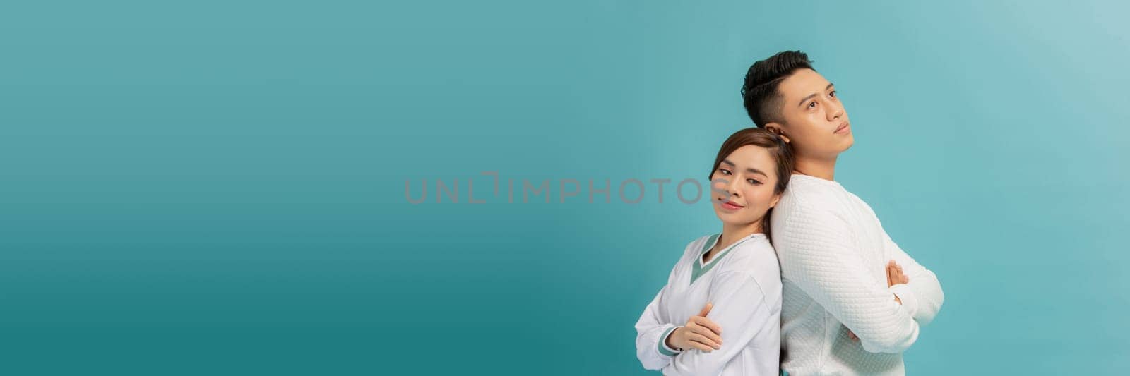 couple man and woman standing back to back with arms crossed isolated over blue banner