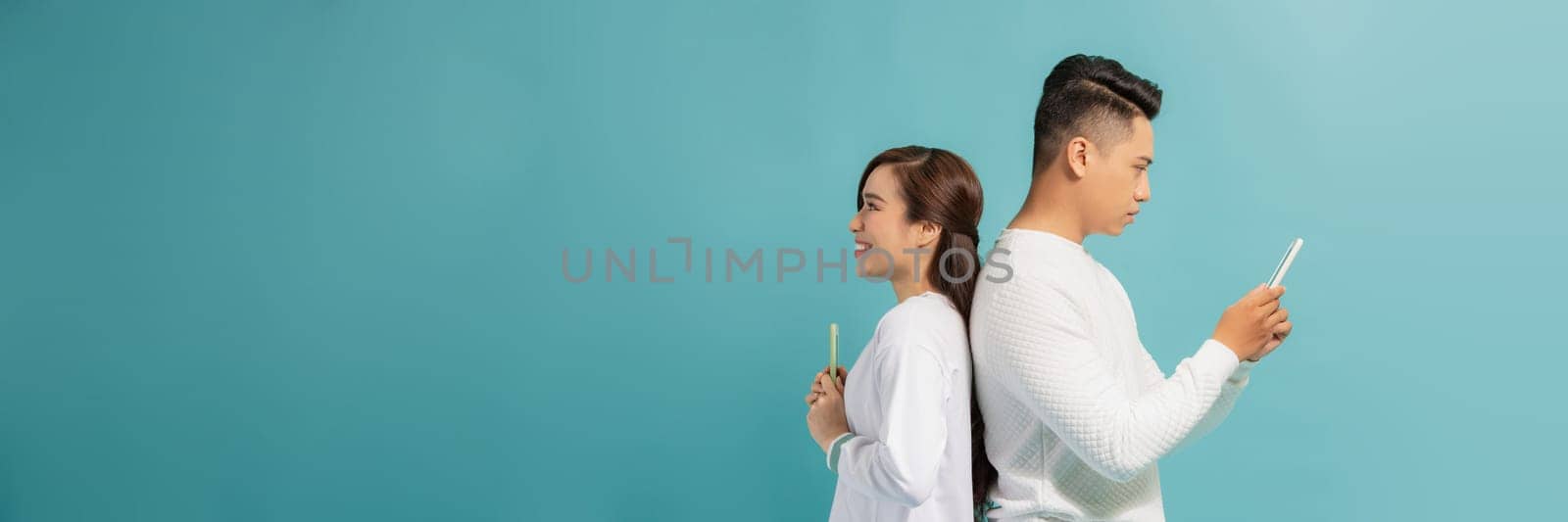 Young Asian woman with man standing on blue while using smartphone and waiting for attention