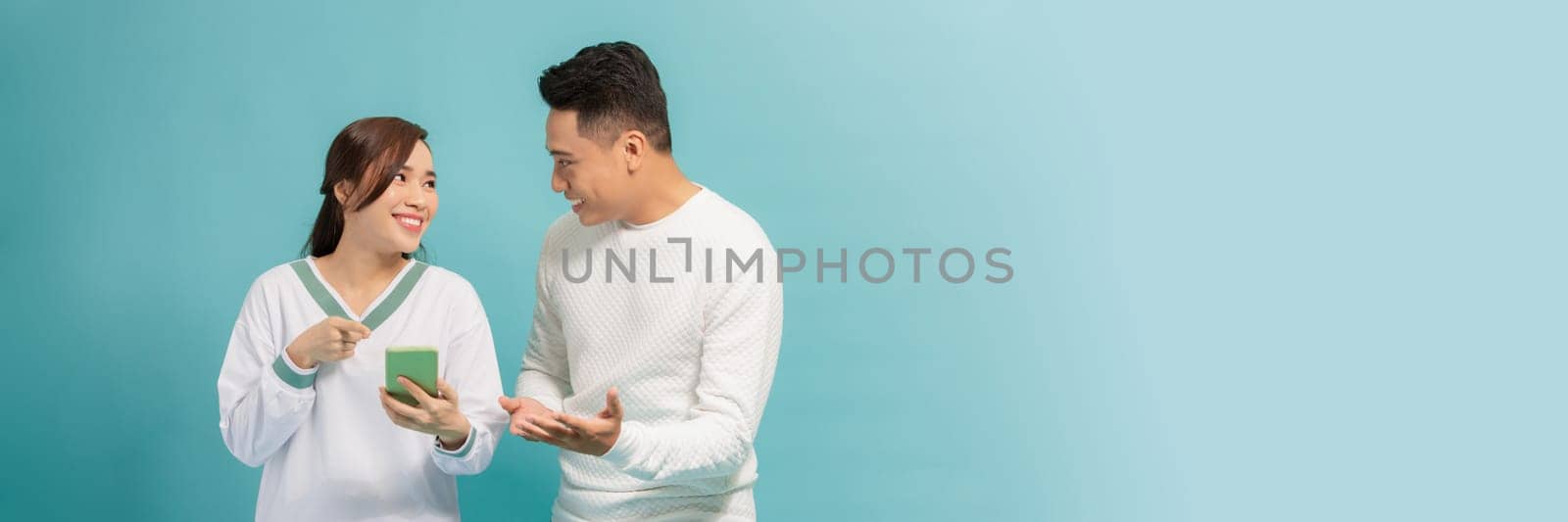 Amazed attractive young Asian couple looking at smartphone together isolated on blue background by makidotvn