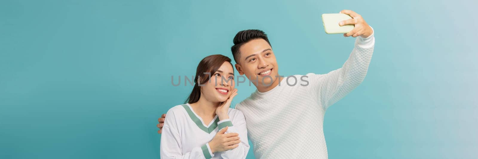A loving young asian couple hugging while standing together and taking a selfie on banner