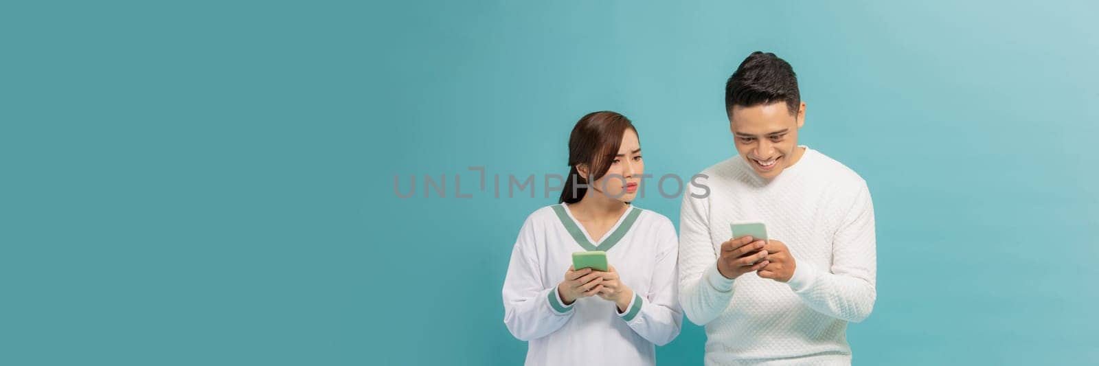 Asian young girl spying on her partner's mobile phone in blue background