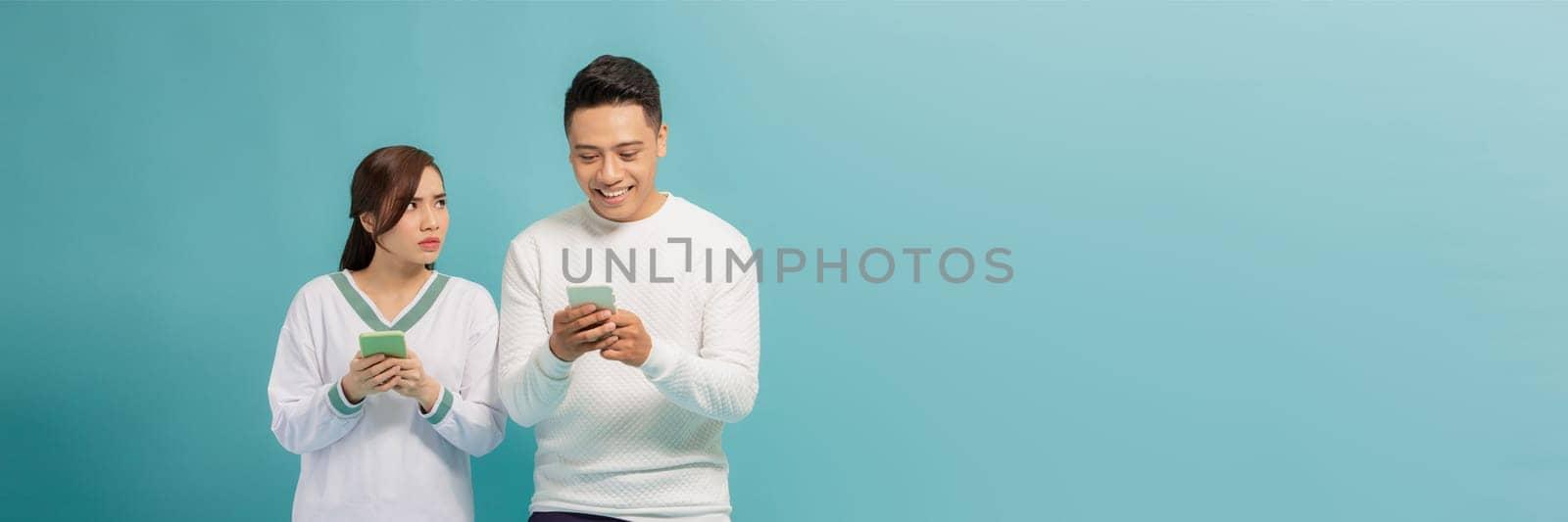 Asian young girl spying on her partner's mobile phone in blue background