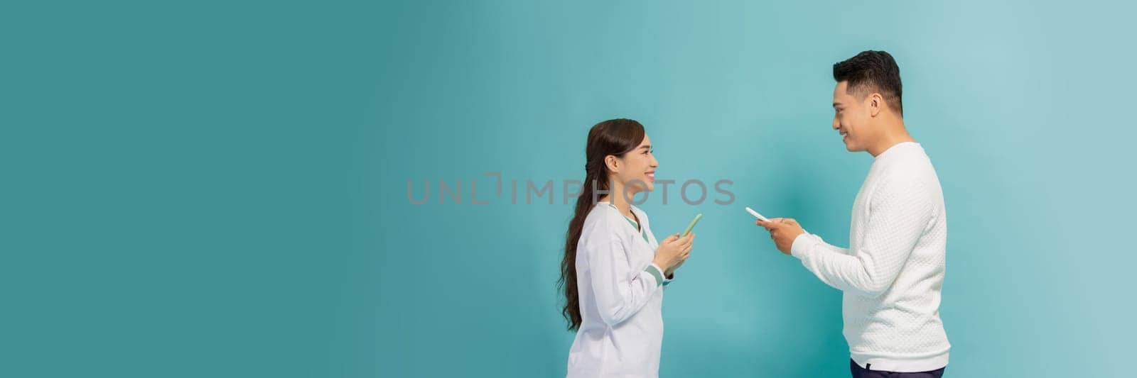 Asian girl and guy using phones sending and reading messages, standing against blue background facing each other by makidotvn