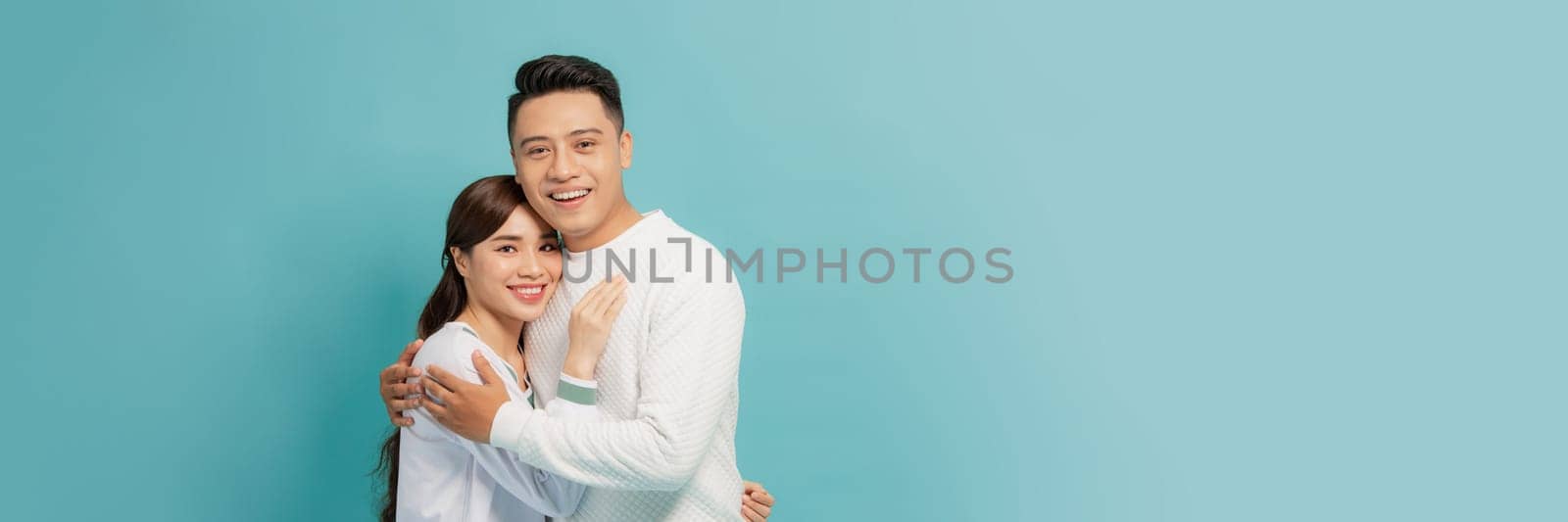 smiling young couple hugging and looking at camera, isolated on blue
