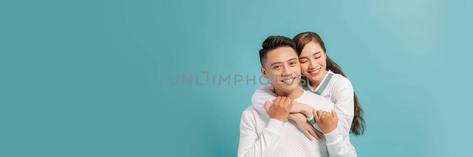 Attractive couple embracing and smiling on turquoise background