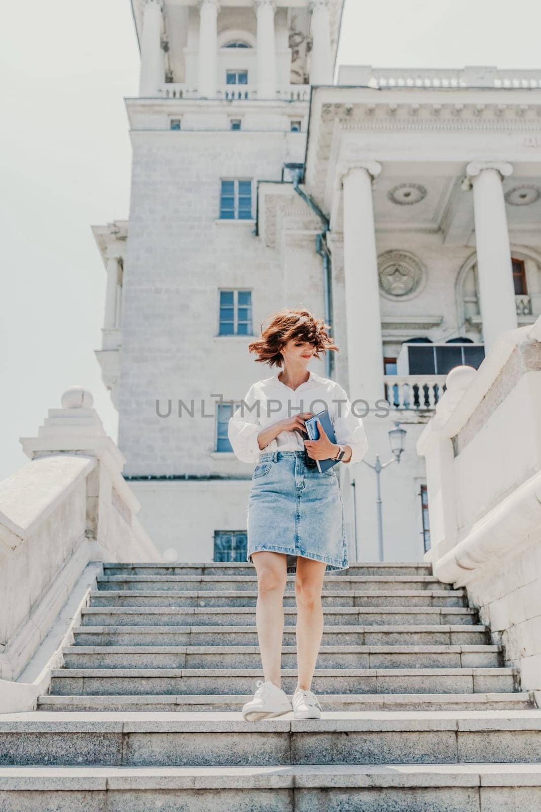 Woman staircase city. A business woman in a white shirt and denim skirt walks down the steps of an ancient building in the city by Matiunina