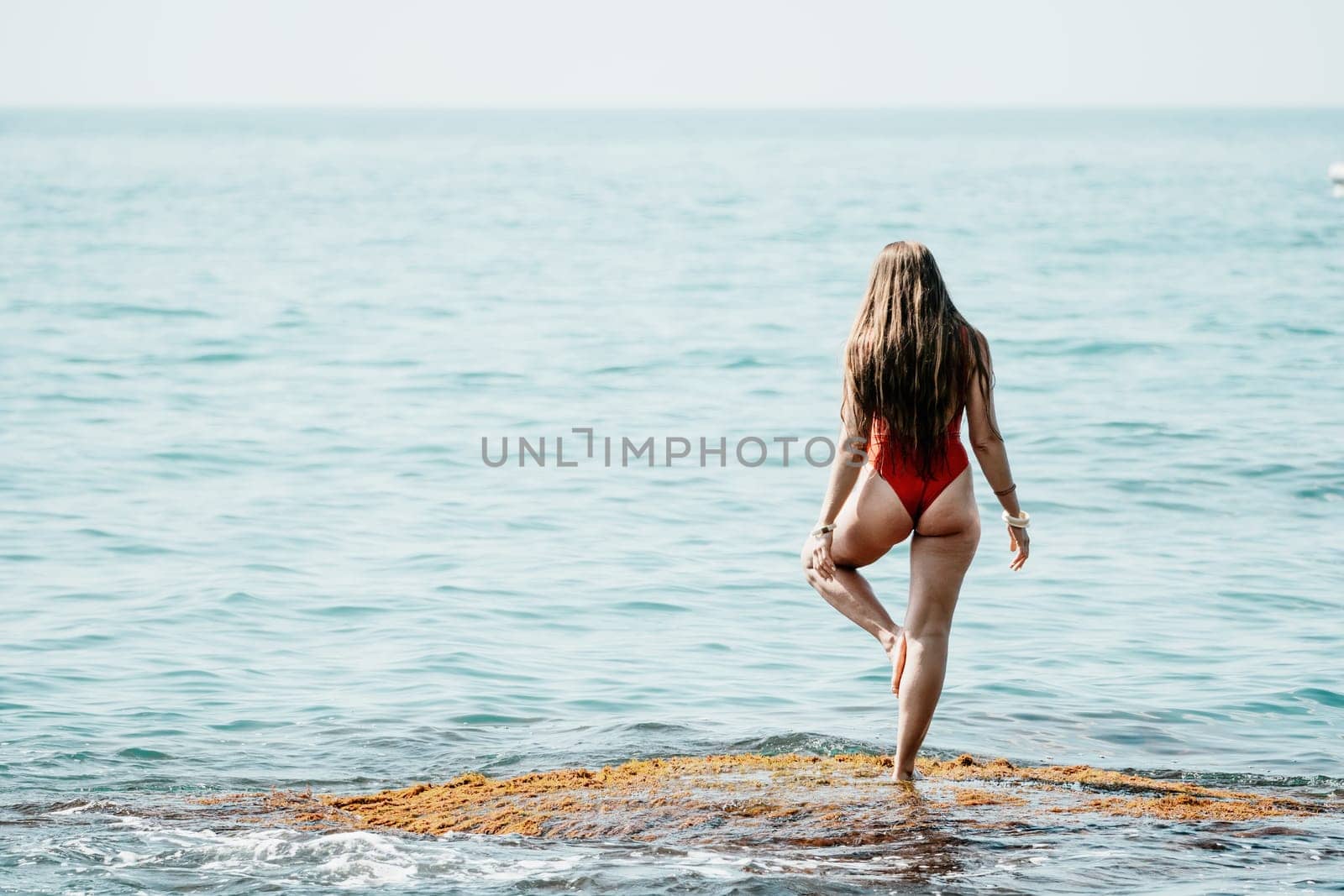 Woman sea yoga. Back view of free calm happy satisfied woman with long hair standing on top rock with yoga position against of sky by the sea. Healthy lifestyle outdoors in nature, fitness concept.