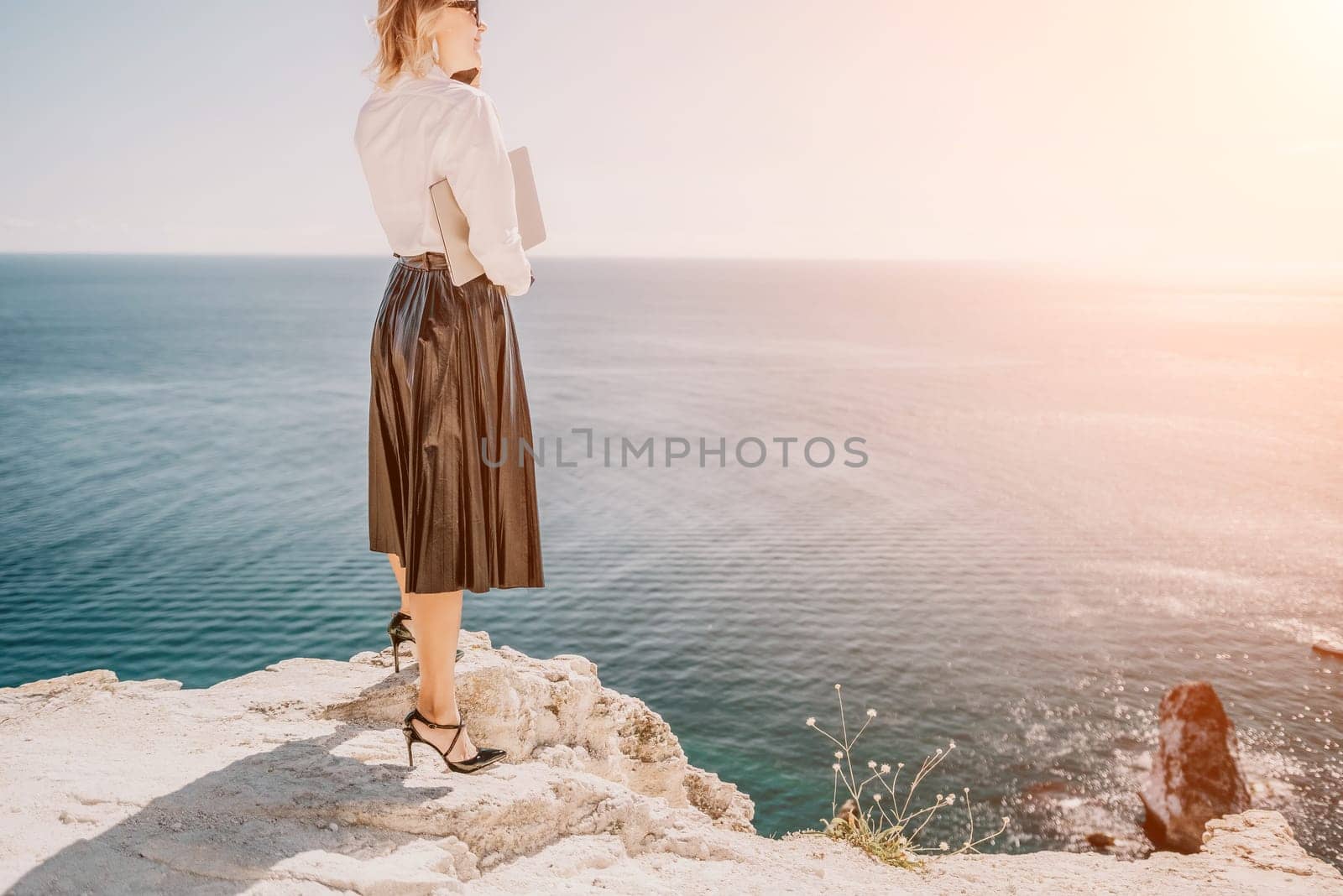 Digital nomad, Business woman working on laptop by the sea. Pretty lady typing on computer by the sea at sunset, makes a business transaction online from a distance. Freelance, remote work on vacation by panophotograph