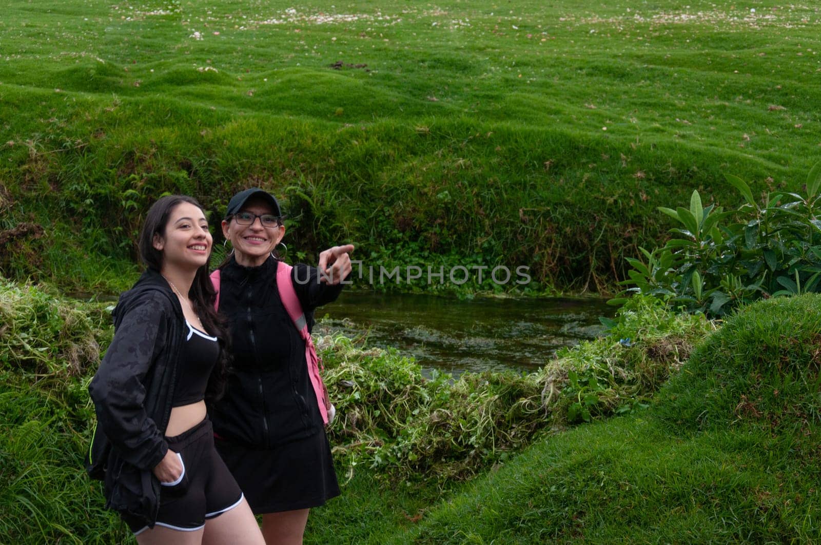 copyspace of mother pointing out a path to her daughter on a grassy green landscape next to a river. backpackers' day. High quality photo