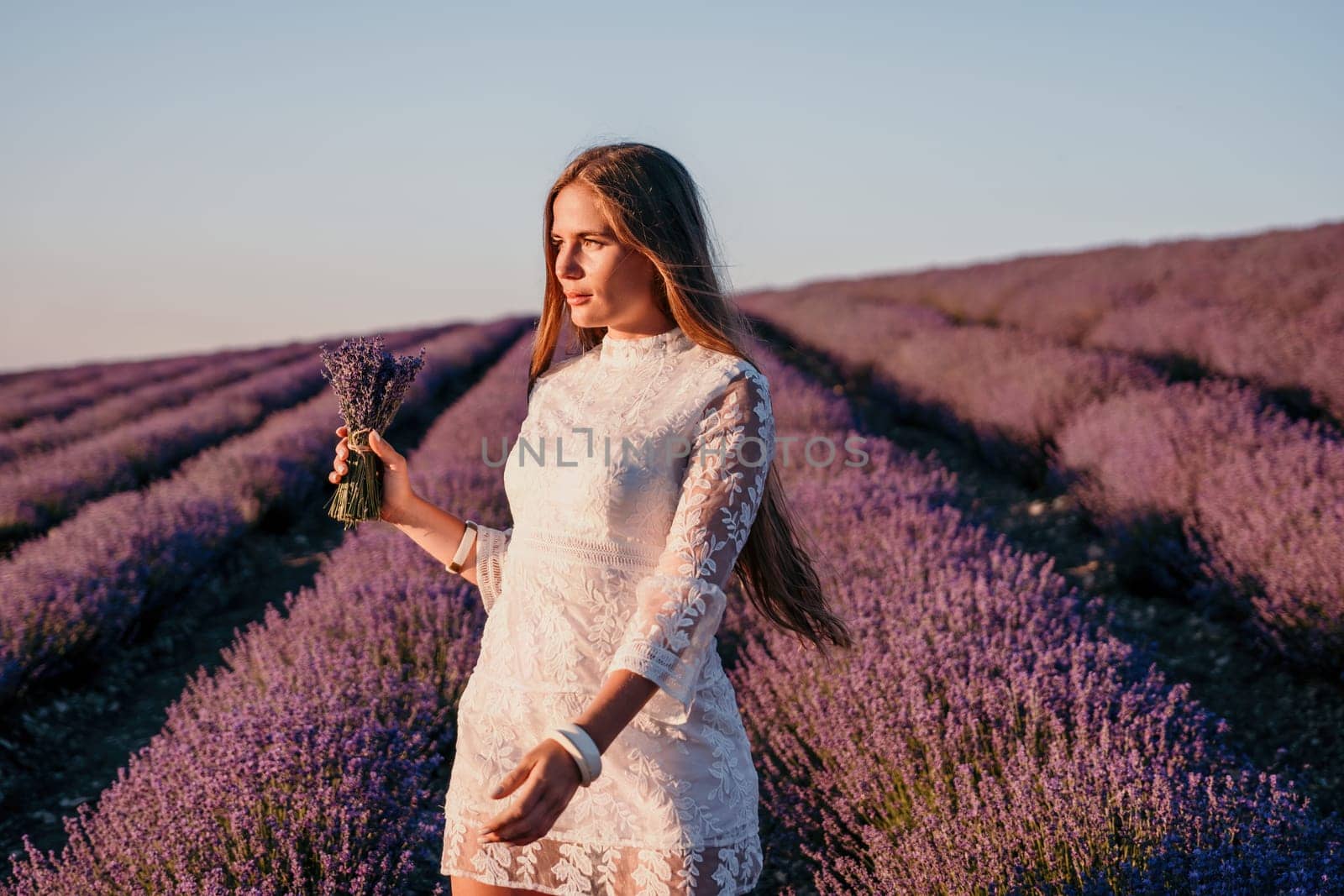 Woman lavender field. Happy carefree woman in a white dress walking in a lavender field and smelling a lavender bouquet on sunset. Ideal for warm and inspirational concepts in wanderlust and travel. by panophotograph