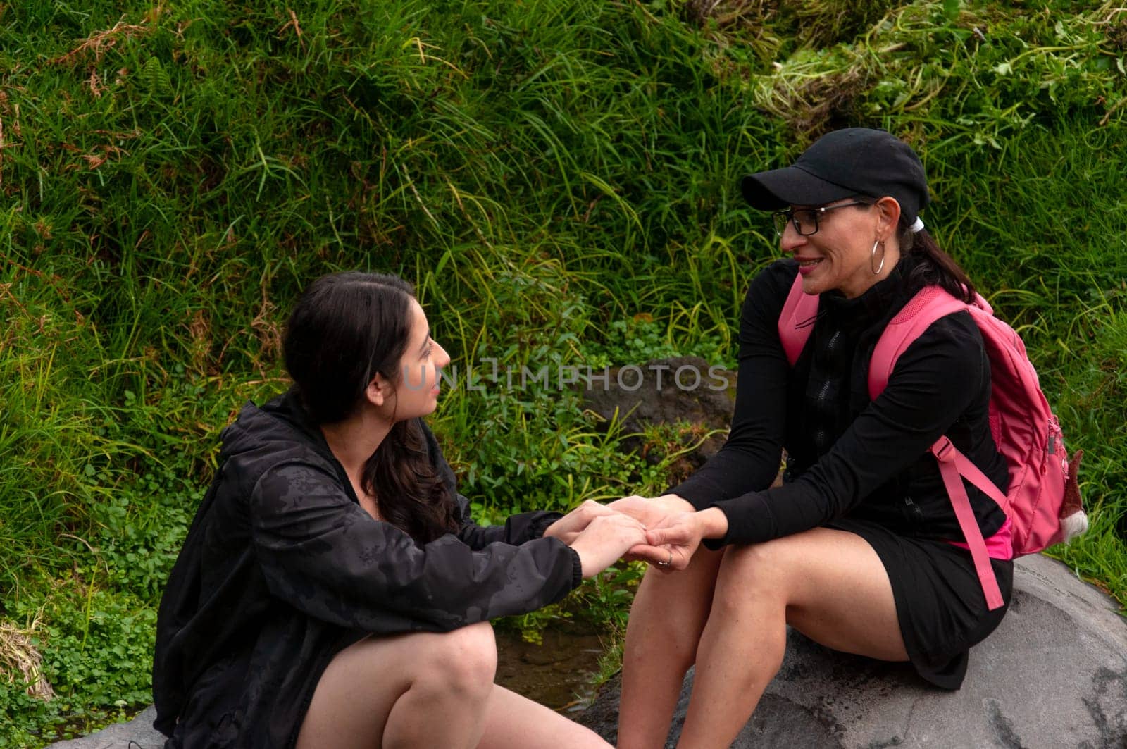 mother and daughter sitting on two rocks looking at each other's eyes while holding hands in an intimate moment between women. women's day. High quality photo