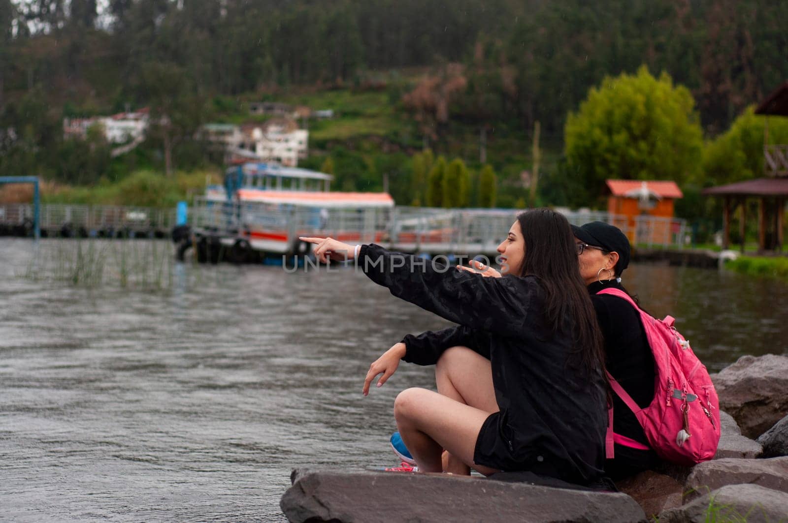 two friends sitting on a wet rock on the shore of a lagoon full of water and one of them pointing to the horizon. backpacker's day. High quality photo
