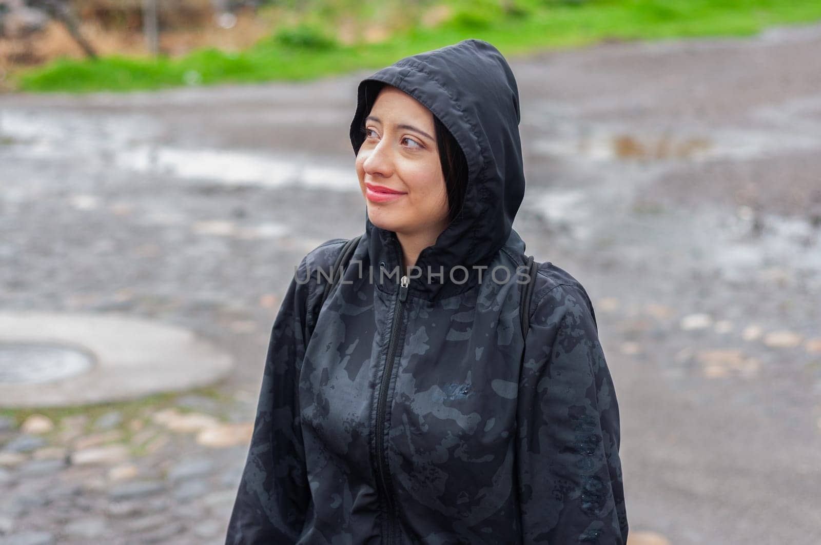 young tourist on a rainy day in a black hooded jacket looking around with a blank stare and a small smile. tourism day. High quality photo